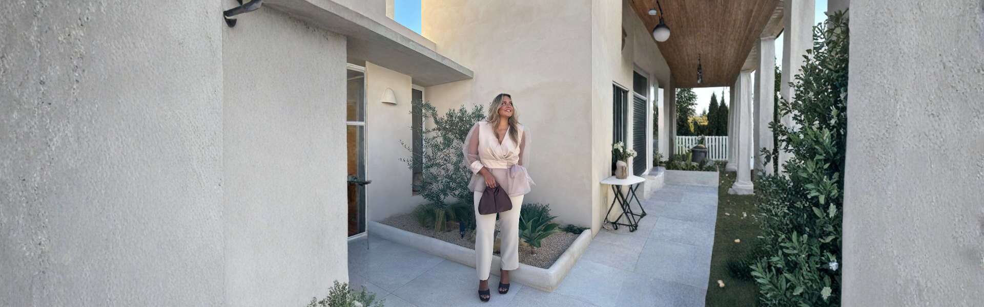 Modelo luciendo un vestido elegante en la entrada de una casa moderna, disfrutando de descuentos hasta el 50.