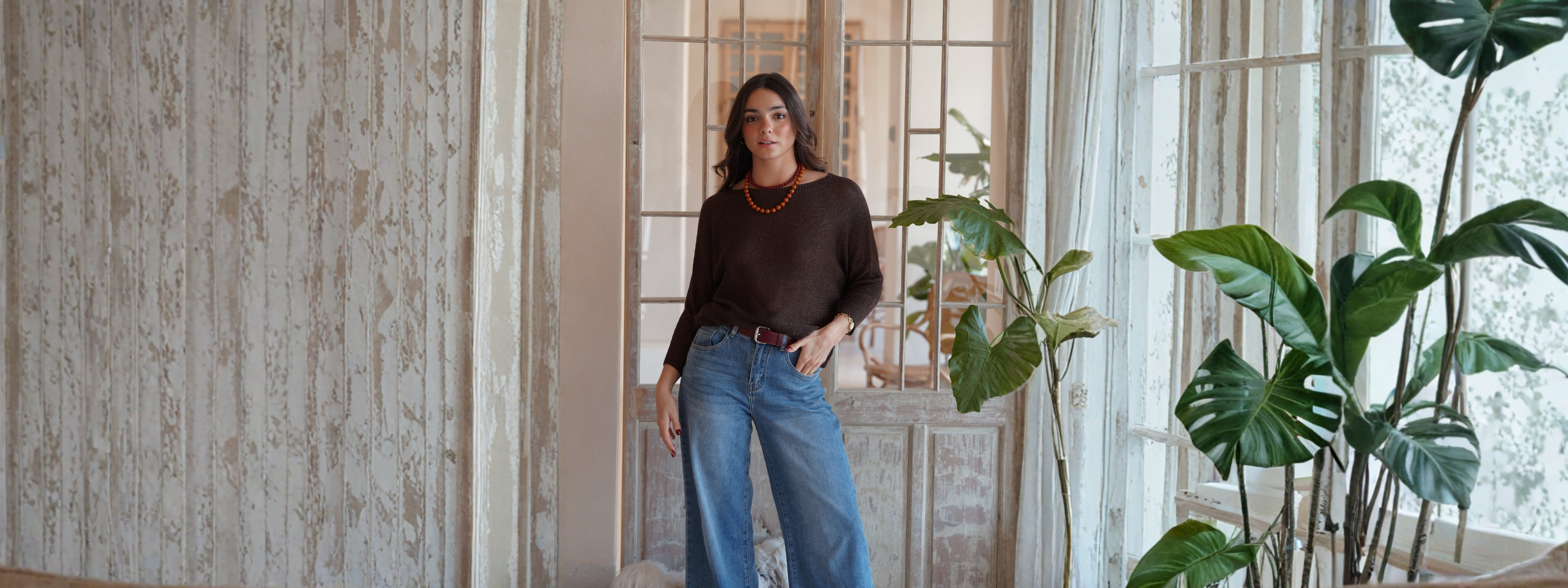 Mujer luciendo un jerséi marrón y jeans anchos en un ambiente luminoso con plantas, parte de la colección Jers.