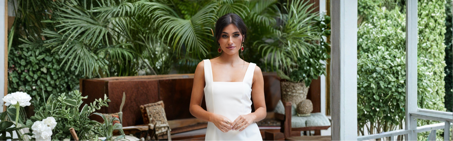 Modelo elegante de vestidos de invitada en un entorno natural con plantas, lista para una boda o evento especial.