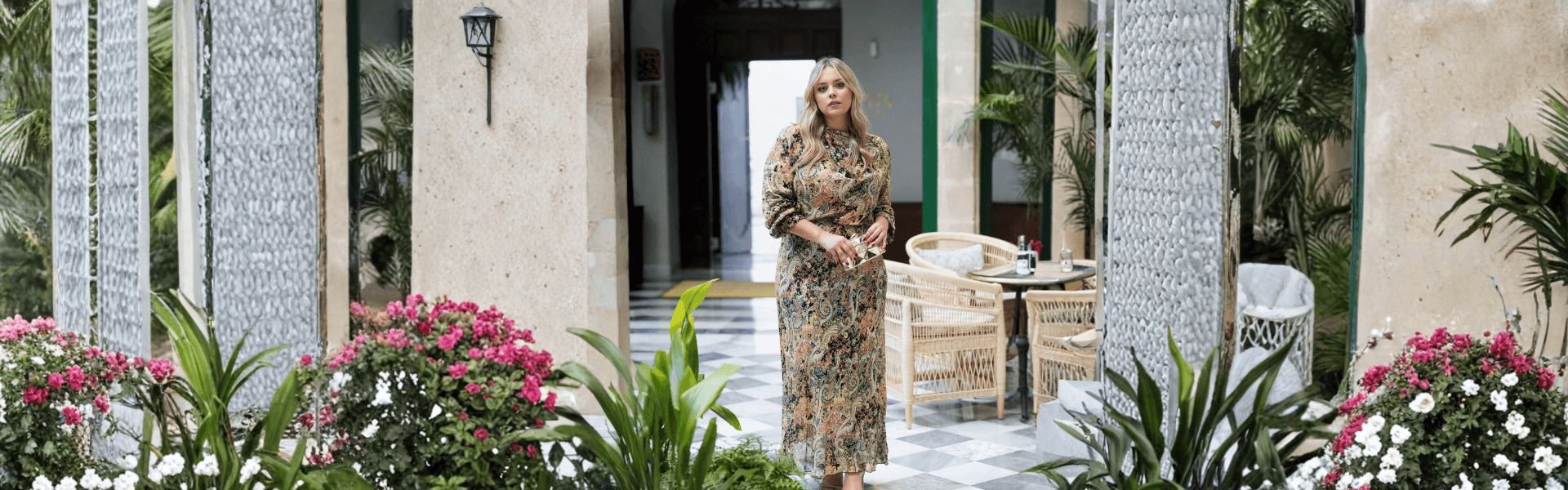 Mujer posando en un patio con flores, luciendo un vestido de fiesta para bodas.