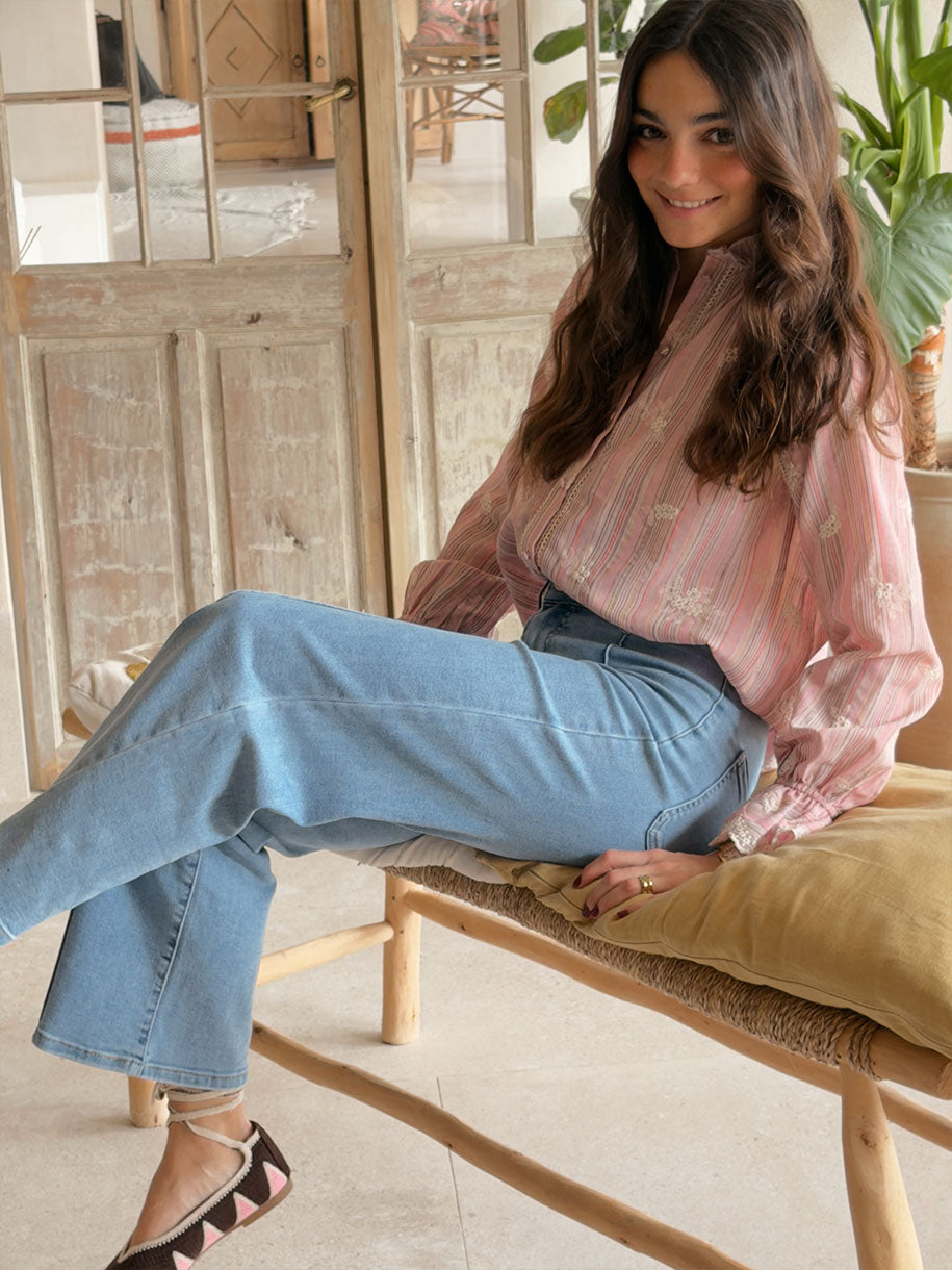 Mujer feliz luciendo la CAMISA RAYAS BORDADAS ROSA, combinación con jeans, en un ambiente luminoso.